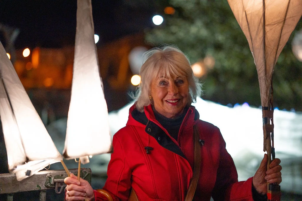 Smiling woman enjoys Mayo Dark Sky Festival night with lanterns in hand, dressed warmly in red.