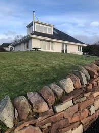 Hilltop house at Mayo Dark Sky Festival, surrounded by green grass and stone wall, under blue sky.