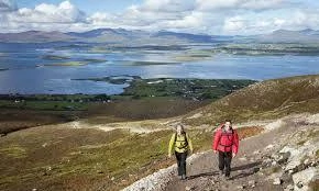 Hikers trek through scenic Mayo mountains with a stunning lakeside view, ideal for the Mayo Dark Sky Festival experience.