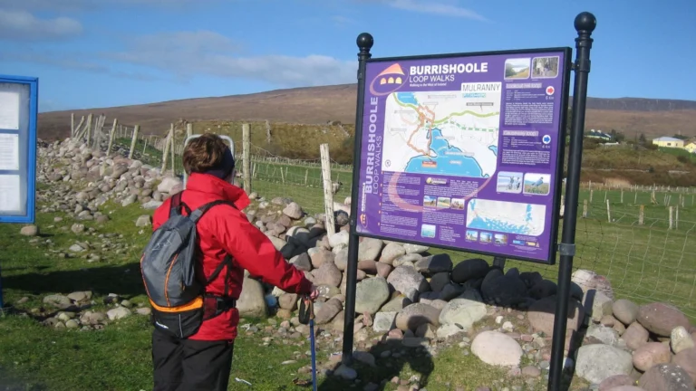 Person in red jacket views Burrishoole Loop Walks sign in scenic Mayo, Ireland. Ideal for Mayo Dark Sky Festival visitors.