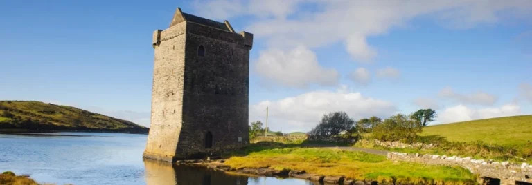 Medieval stone tower beside tranquil lake under blue sky in County Mayo, Ireland, site of Dark Sky Festival.