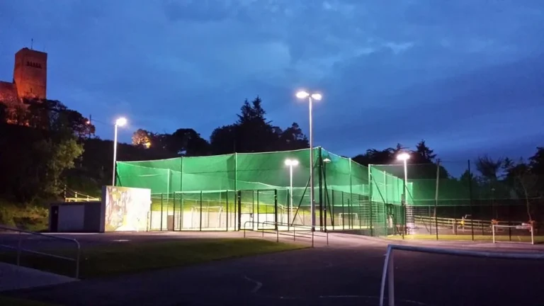Lit sports court at dusk with surrounding trees and a building, highlighting Mayo Dark Sky Festival atmosphere.
