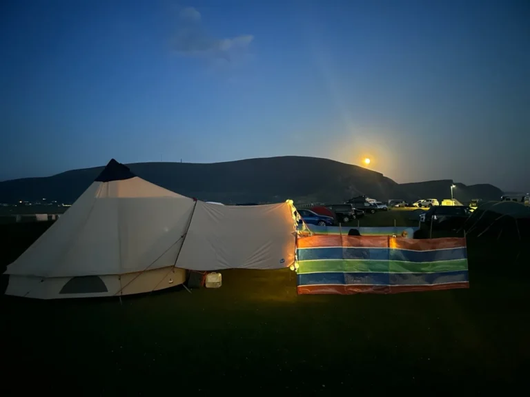 Camping under a starry sky with a glowing sunset at Mayo Dark Sky Festival, highlighting tents and tranquil hills.