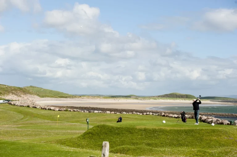 Golfer on a scenic coastal course in Mayo, Ireland, under a bright blue sky at the Mayo Dark Sky Festival site.