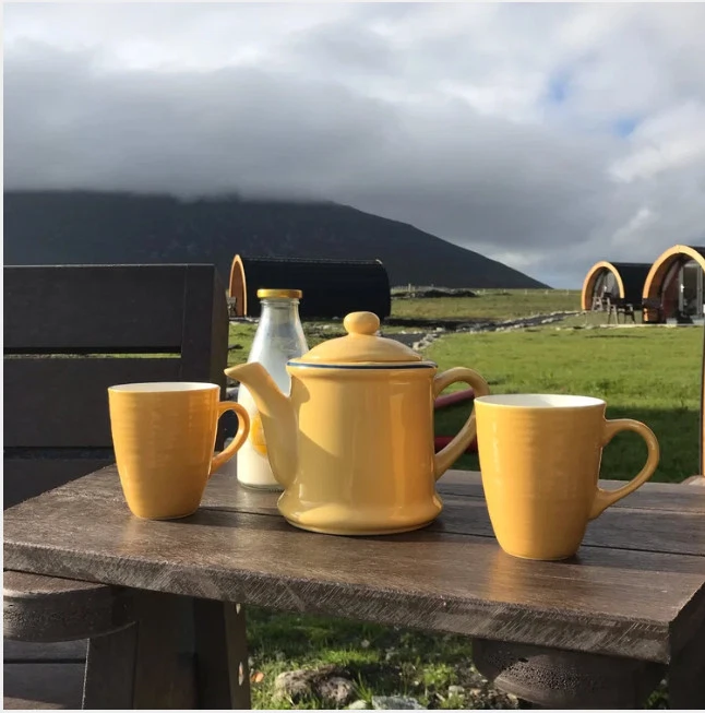 Tea set with yellow pots and cups on a table outdoors, Mayo Dark Sky Festival cabins in the background.