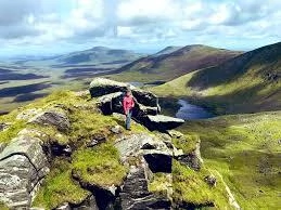 Scenic view from Mayo Dark Sky Festival, showcasing a hiker on a rugged peak with sprawling landscapes and distant hills.
